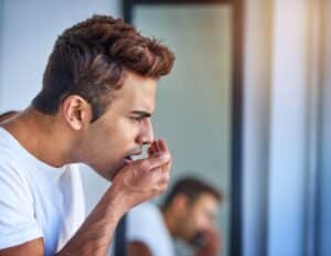 Man checking his breath in the bathroom, concerned about bad breath caused by potential gum disease or gingivitis. Emphasis on oral hygiene and halitosis prevention as part of a morning routine.