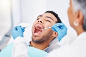 Dentist examining a male patient's teeth with a mirror and tools, highlighting deep dental cleaning, plaque, tartar removal, and oral health care.